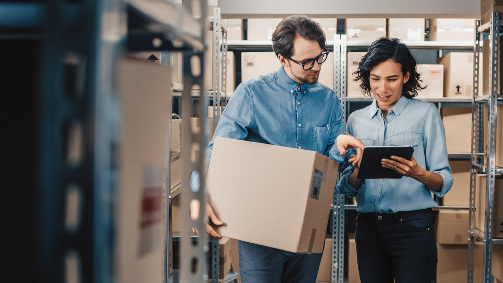 Two workers in a warehouse checking inventory and order status on a tablet