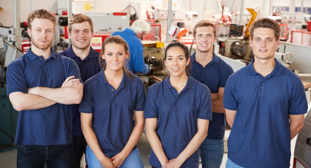 A team of young employees in a workshop wearing matching professional uniforms and custom company shirts, representing branded apparel and employee uniforms.