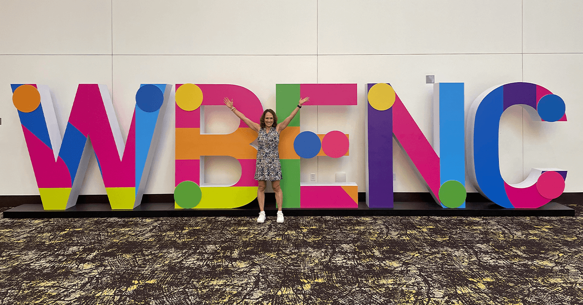 A certified woman business owner stands with arms raised in front of large, colorful letters spelling "WBENC" (Women's Business Enterprise National Council), representing the benefits and national importance of WBE certification for supplier diversity in procurement.